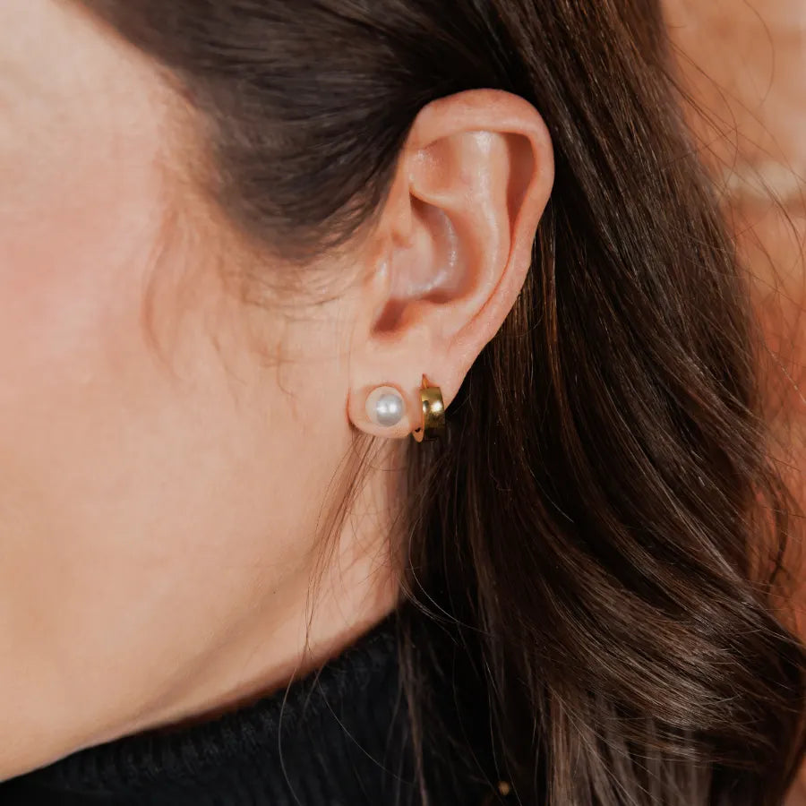 Oreille portant une boucle d'oreille Caracol perle et un anneau doré épais