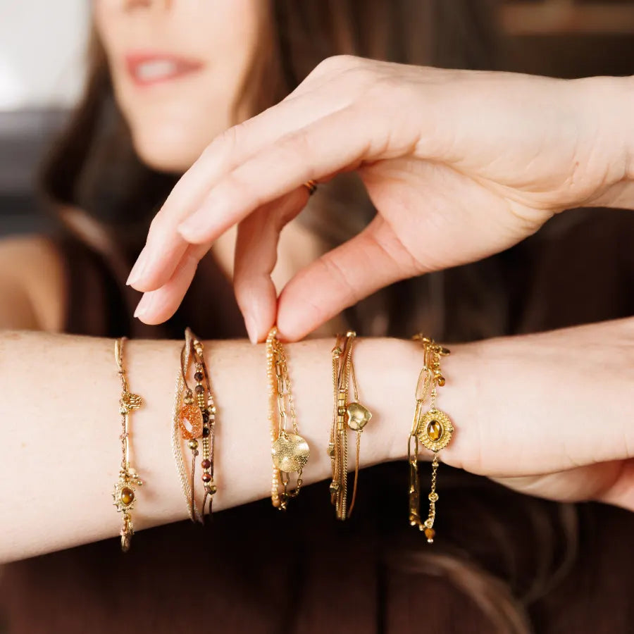 Poignet portant plusieurs bracelets joncs et chaînes Caracol dorés empilés