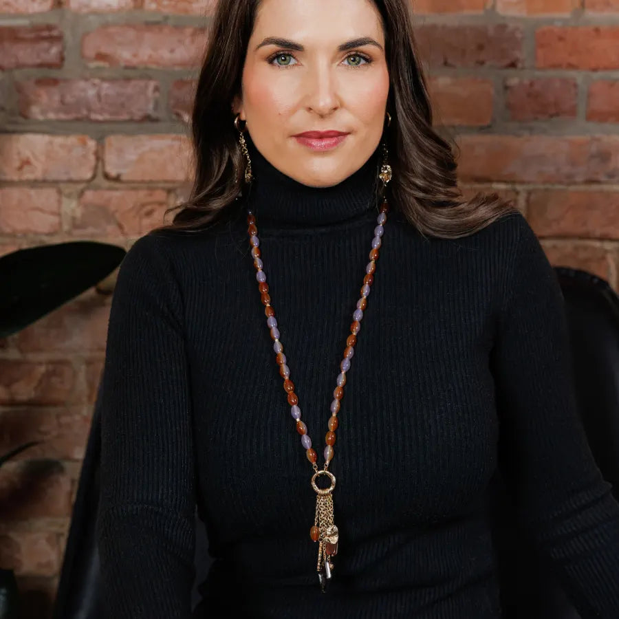 Woman wearing a long Caracol beaded necklace in amber and lilac with a tassel pendant