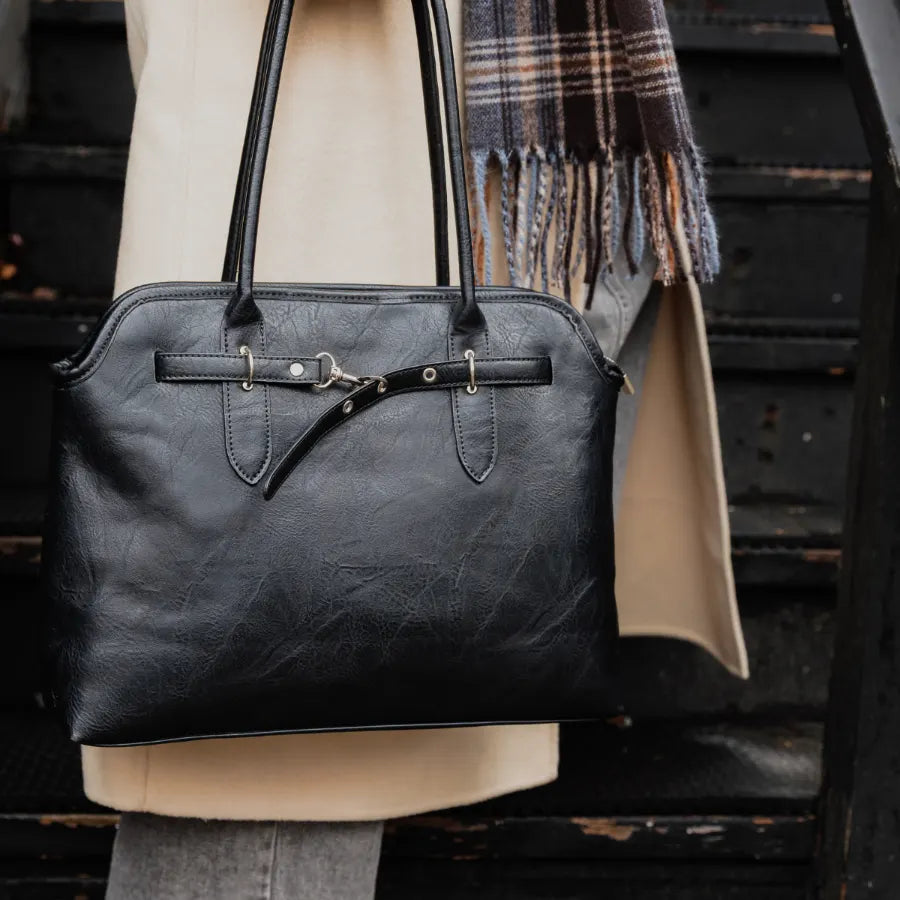 Sac à main Caracol noir porté à l'épaule avec un manteau beige et un foulard à carreaux