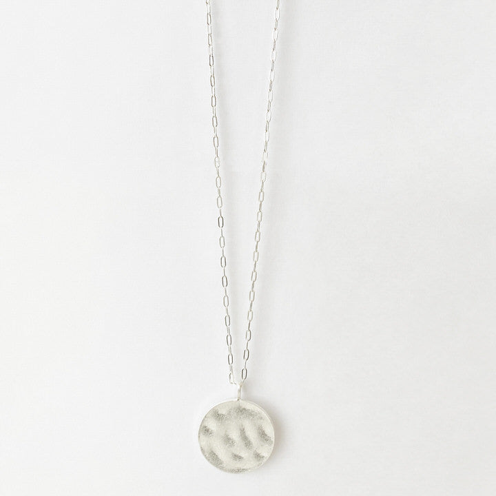 LONGUE CHAÎNE AVEC PENDENTIF ROND MÉTALLIQUE MARTELÉ AU FINI USÉ - ARGENT | LONG NECKLACE ON CHAIN WITH WORN HAMMERED METAL ROUND PENDANT - SILVER